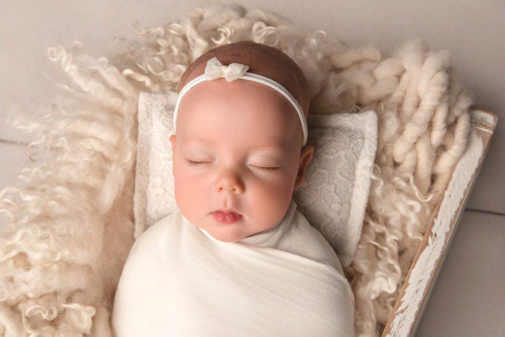 baby girl with white bow sleeps on pillow in wooden box